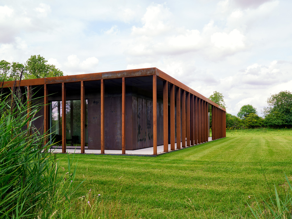 Modern building with rusted facade in green field.