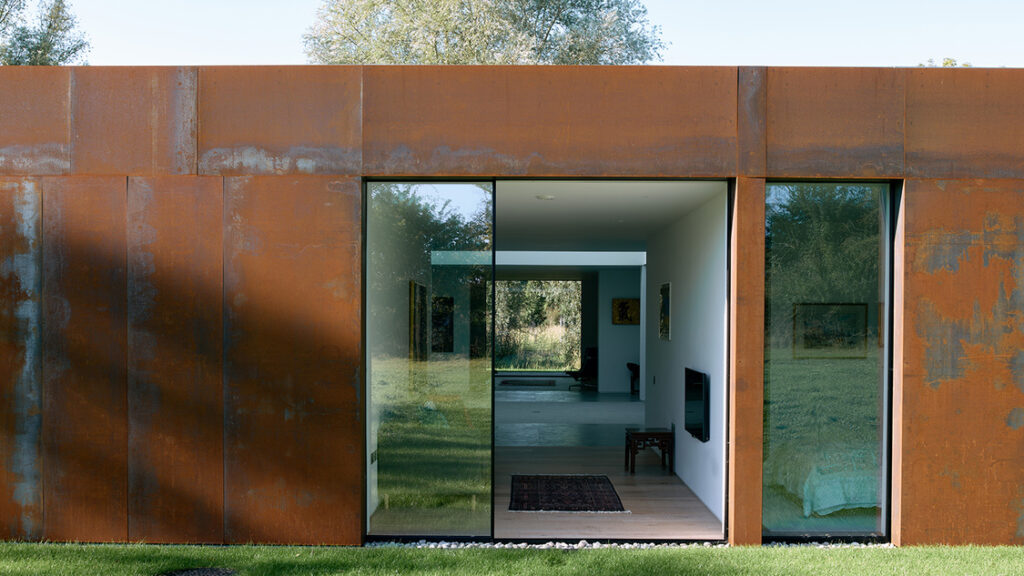 Modern rusted steel house with large glass windows.